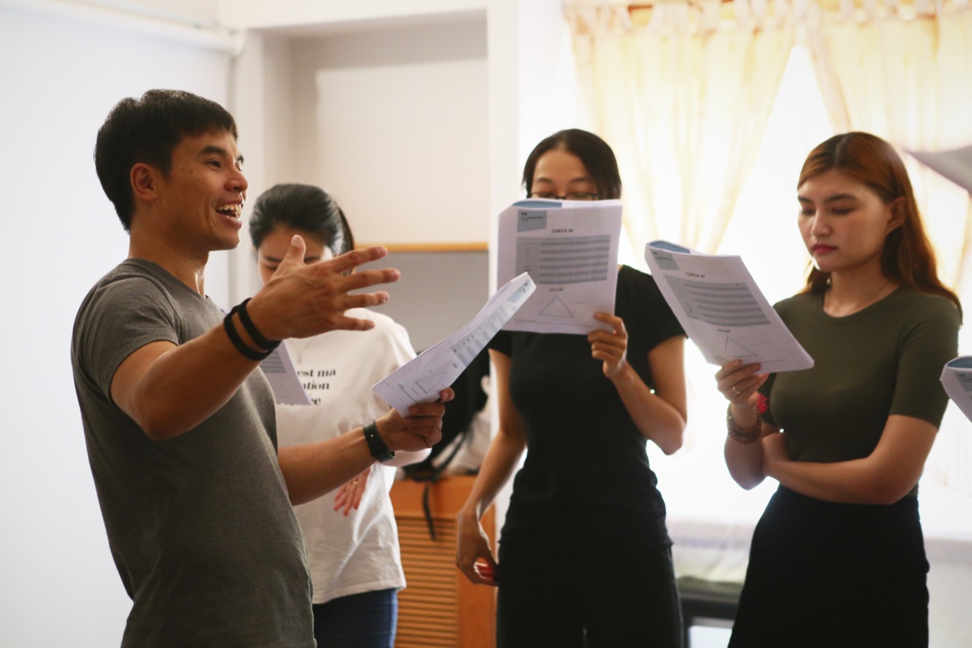 Derrick working with a small group in a bright room, everyone standing with scripts in hand